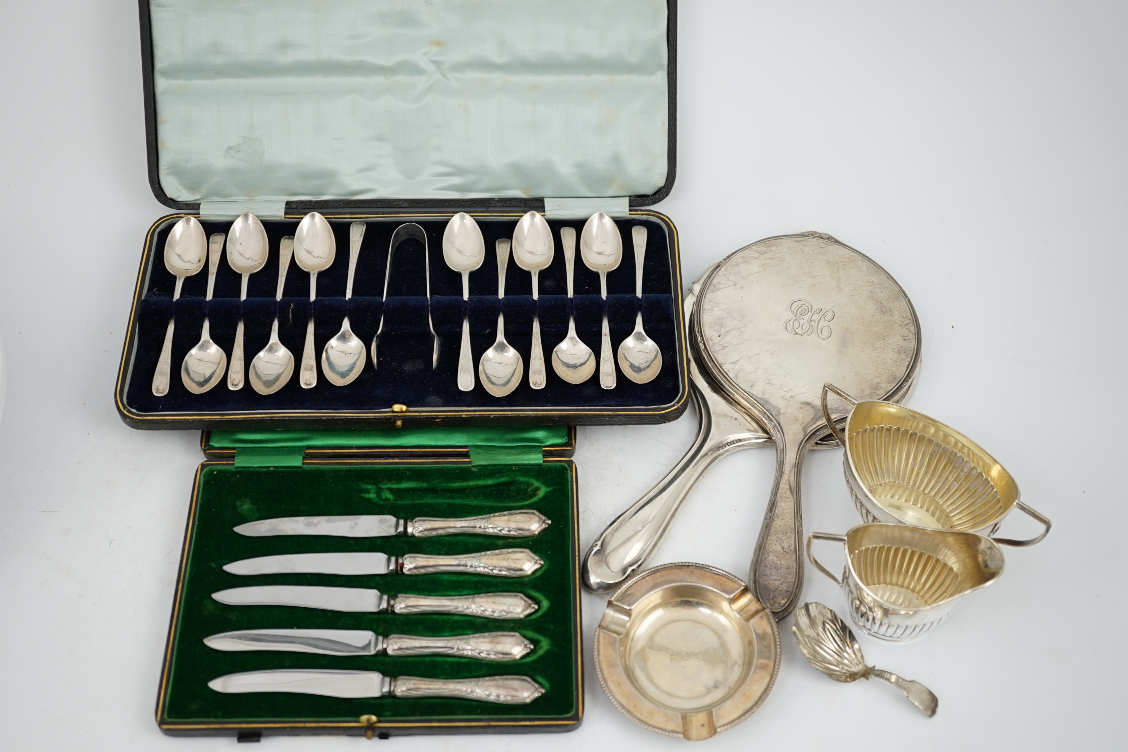 A cased set of twelve George V silver teaspoons with sugar tongs, Sheffield, 1912, two silver hand mirrors, a silver sugar bowl and cream jug, a silver ashtray, a George III silver caddy spoon and cased plated tea knives